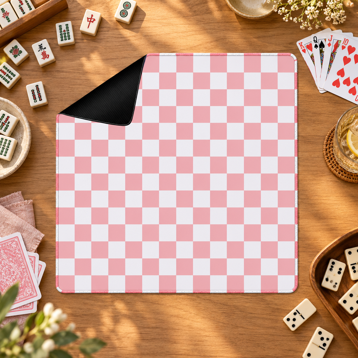 Checker pink mahjong mat with mahjong tiles, playing cards and dominoes as props outside the mat
